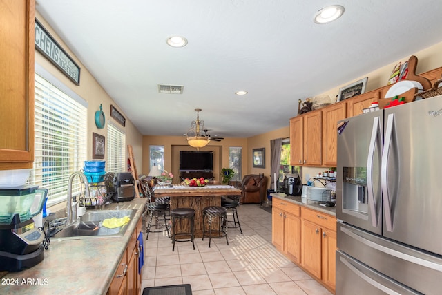 kitchen featuring light tile patterned floors, decorative light fixtures, sink, stainless steel fridge with ice dispenser, and a breakfast bar