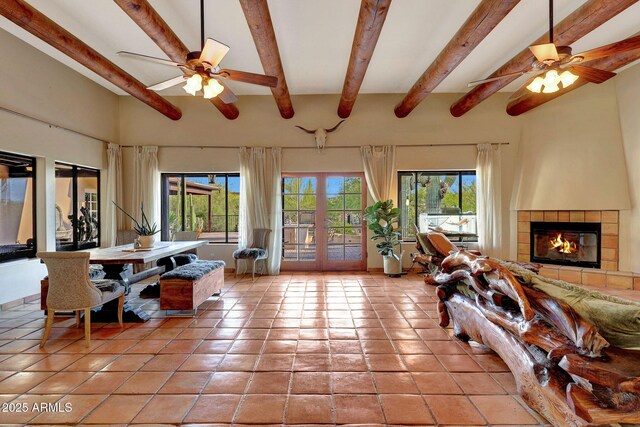 living area with ceiling fan, light tile patterned floors, beamed ceiling, a tile fireplace, and french doors