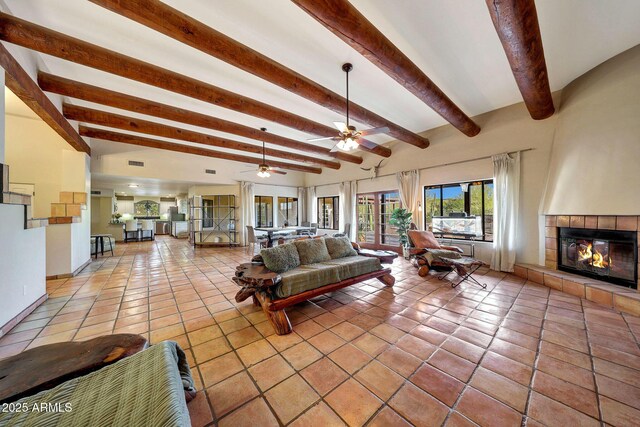 living room with beamed ceiling, a tiled fireplace, ceiling fan, light tile patterned flooring, and baseboards