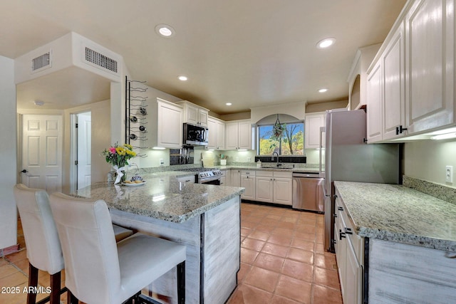 kitchen featuring appliances with stainless steel finishes, a peninsula, white cabinets, light stone counters, and recessed lighting