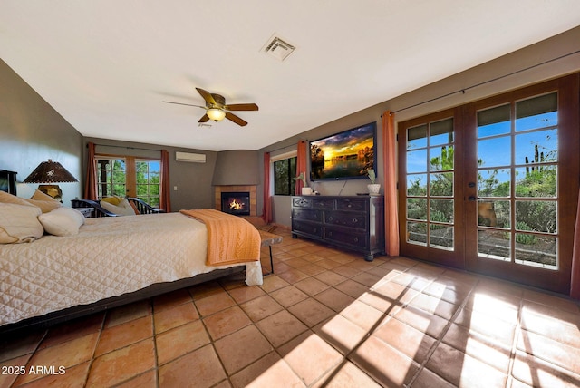 tiled bedroom with french doors, access to outside, a wall unit AC, a tiled fireplace, and ceiling fan