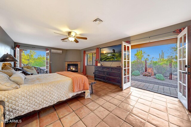 tiled bedroom featuring a wall unit AC, access to exterior, a tiled fireplace, and multiple windows
