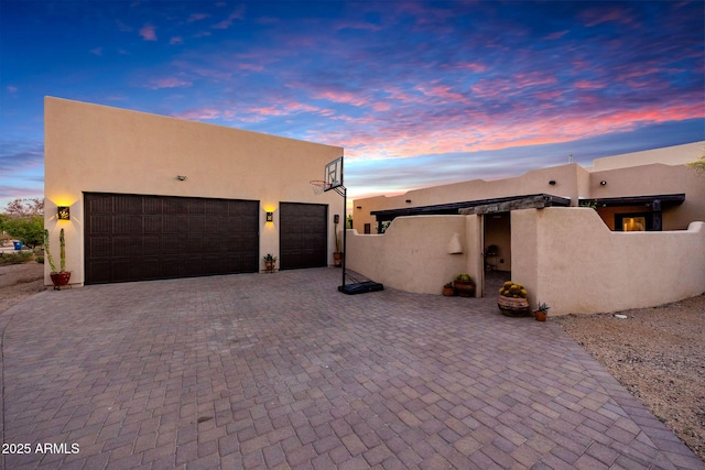 adobe home featuring stucco siding, decorative driveway, a garage, and fence
