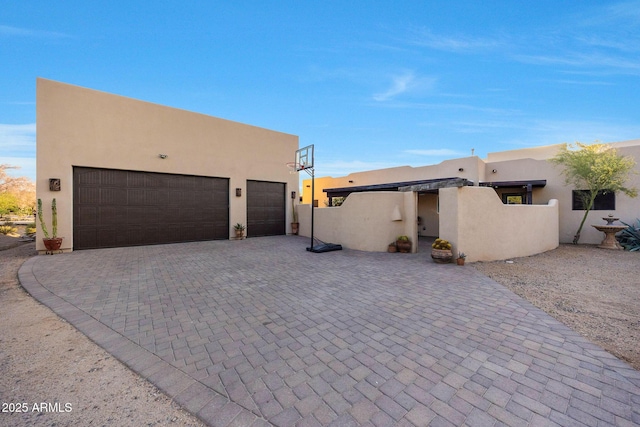 pueblo revival-style home featuring stucco siding, decorative driveway, and a garage