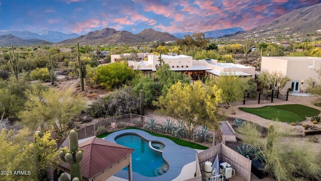 pool at dusk featuring an area to practice putting, a mountain view, a fenced backyard, and a patio area