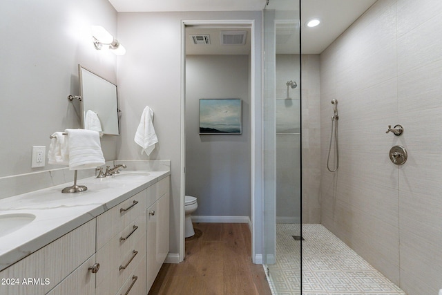 bathroom featuring toilet, vanity, hardwood / wood-style flooring, and a tile shower