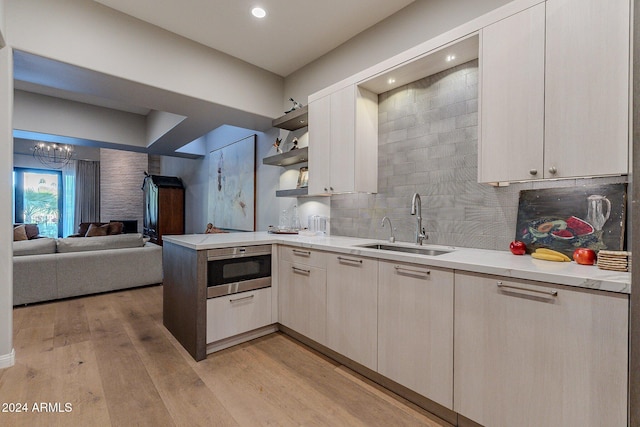 kitchen featuring light hardwood / wood-style floors, an inviting chandelier, kitchen peninsula, sink, and tasteful backsplash