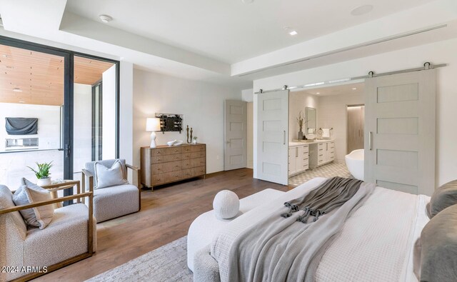 bedroom featuring a barn door, ensuite bath, and wood-type flooring