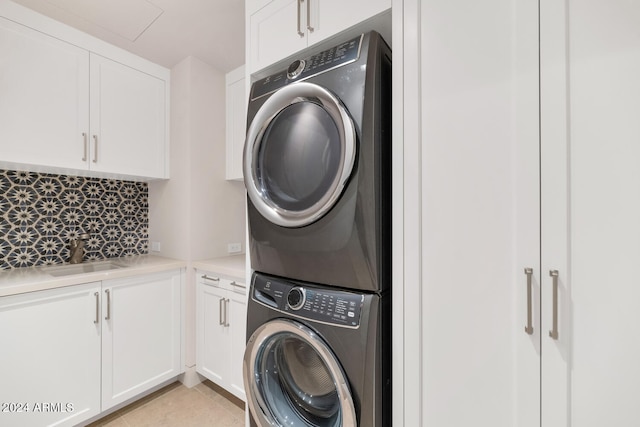 clothes washing area featuring stacked washing maching and dryer, sink, light tile flooring, and cabinets