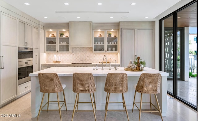 kitchen featuring light tile flooring, gas cooktop, tasteful backsplash, an island with sink, and sink