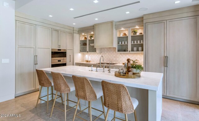 kitchen with a center island with sink, light stone counters, a kitchen bar, tasteful backsplash, and light tile floors