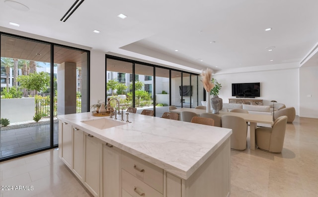 kitchen featuring white cabinets, a center island with sink, expansive windows, and sink