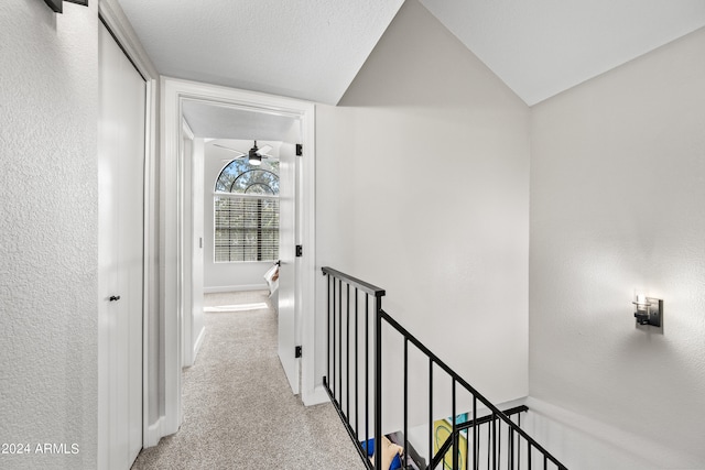 corridor with lofted ceiling, a textured ceiling, and light colored carpet