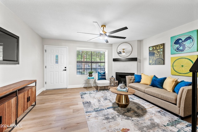 living room with a textured ceiling, ceiling fan, light hardwood / wood-style flooring, and a large fireplace