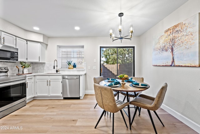 kitchen featuring appliances with stainless steel finishes, hanging light fixtures, white cabinetry, an inviting chandelier, and light hardwood / wood-style flooring