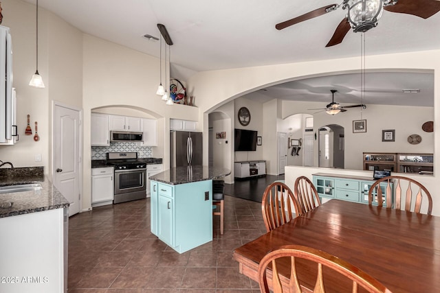 kitchen with vaulted ceiling, a ceiling fan, appliances with stainless steel finishes, white cabinets, and arched walkways