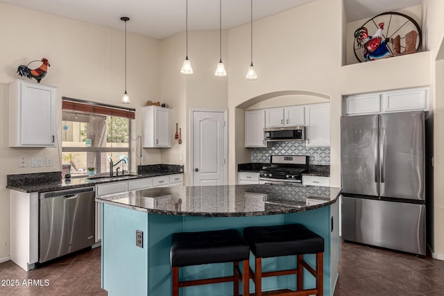kitchen featuring white cabinetry, dark tile patterned floors, a kitchen island, a sink, and appliances with stainless steel finishes