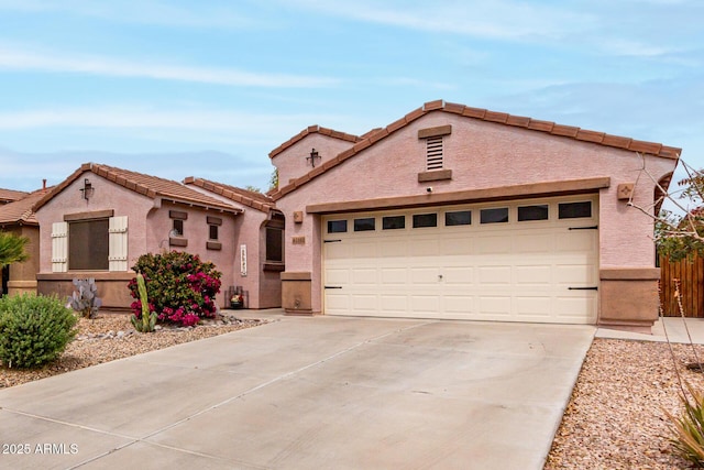 mediterranean / spanish-style home featuring a tile roof, concrete driveway, stucco siding, fence, and a garage