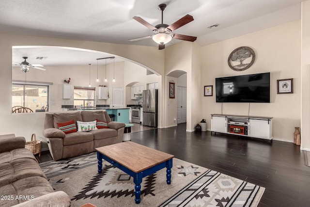 living area featuring lofted ceiling, dark wood-style flooring, arched walkways, visible vents, and a ceiling fan