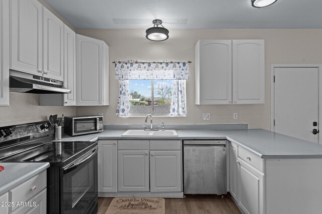 kitchen featuring under cabinet range hood, a peninsula, a sink, white cabinets, and appliances with stainless steel finishes