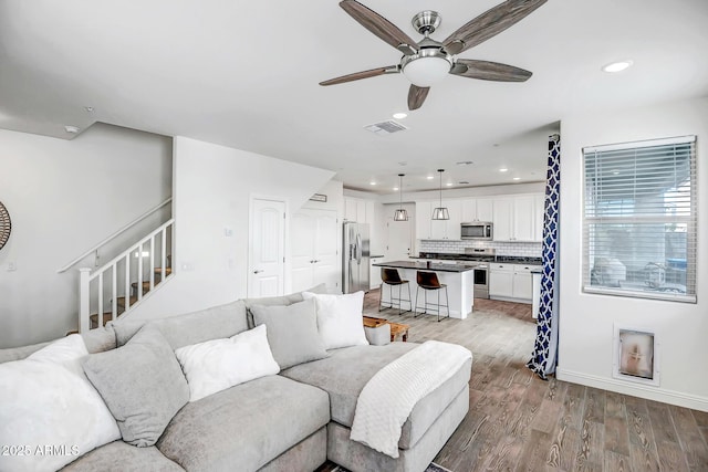 living room with visible vents, light wood-style flooring, a ceiling fan, recessed lighting, and stairway