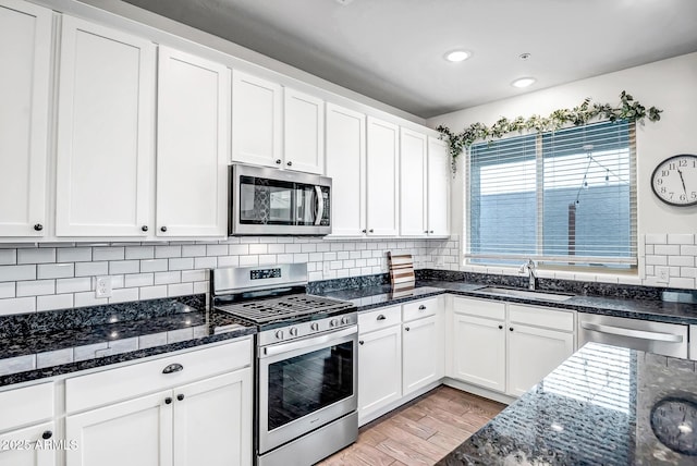 kitchen with dark stone countertops, a sink, appliances with stainless steel finishes, white cabinetry, and tasteful backsplash