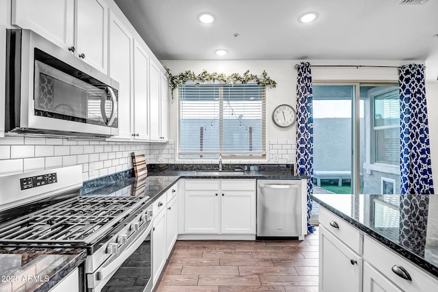 kitchen with wood tiled floor, decorative backsplash, stainless steel appliances, white cabinetry, and a sink