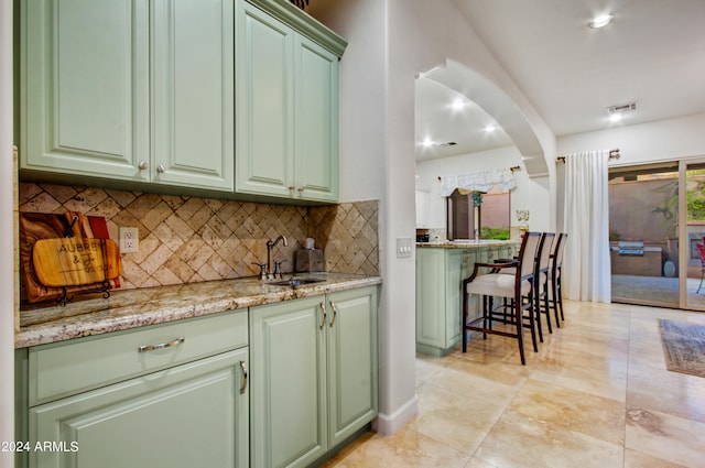 kitchen featuring green cabinetry, light stone countertops, backsplash, and sink