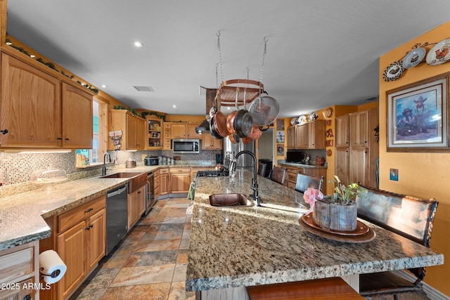 kitchen with light stone countertops, sink, appliances with stainless steel finishes, and an island with sink