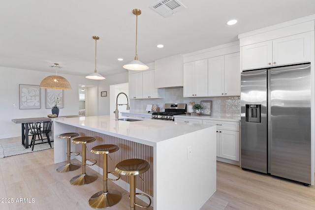 kitchen with light countertops, appliances with stainless steel finishes, a sink, an island with sink, and wall chimney exhaust hood