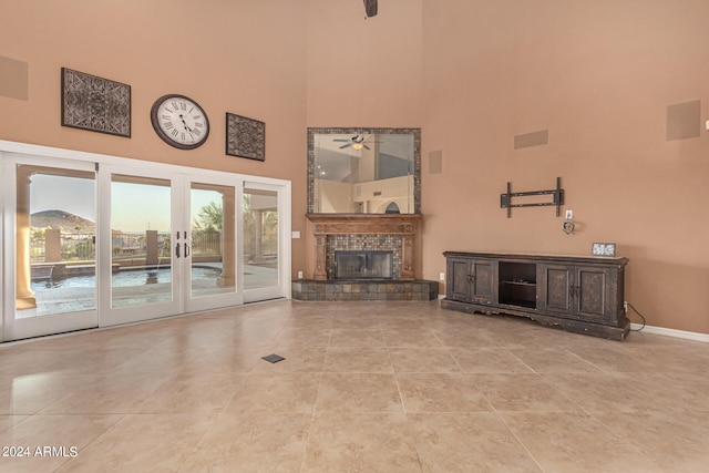 unfurnished living room featuring a tile fireplace, a high ceiling, french doors, ceiling fan, and light tile patterned flooring