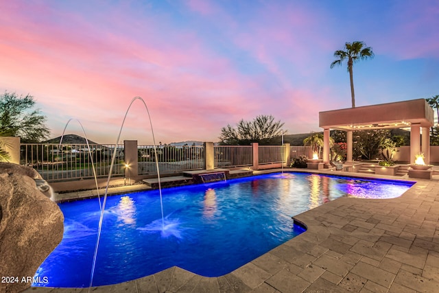 pool at dusk with pool water feature, a patio, and an outdoor fire pit