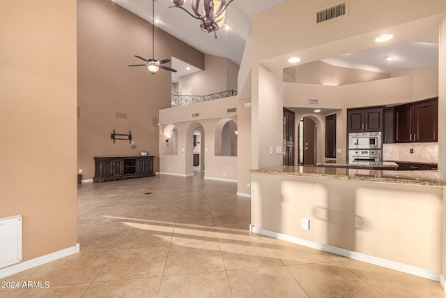 kitchen with ceiling fan with notable chandelier, a towering ceiling, appliances with stainless steel finishes, light tile patterned flooring, and light stone counters