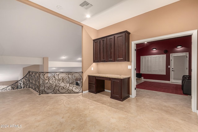 kitchen with dark brown cabinetry, light stone countertops, and lofted ceiling