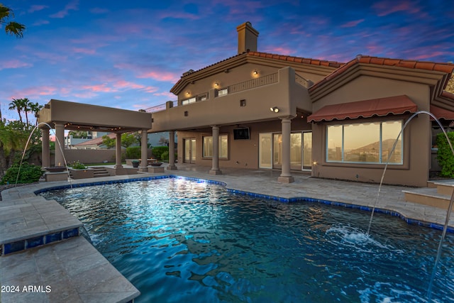 pool at dusk with pool water feature, a patio, and a hot tub