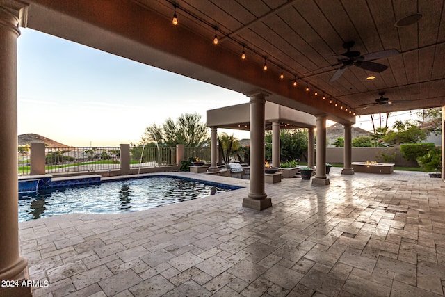 pool at dusk with pool water feature, ceiling fan, and a patio area