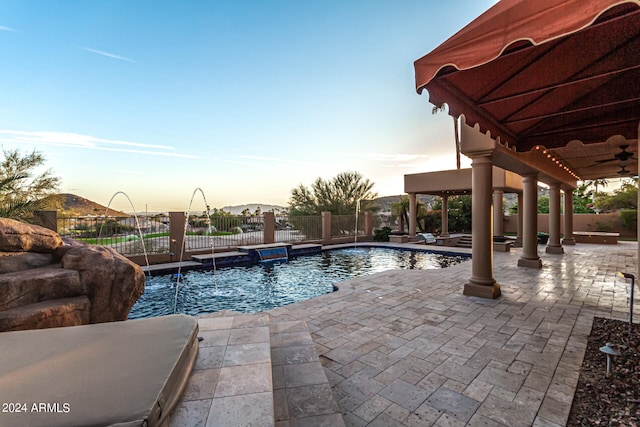 pool at dusk featuring ceiling fan, pool water feature, a patio, and a jacuzzi