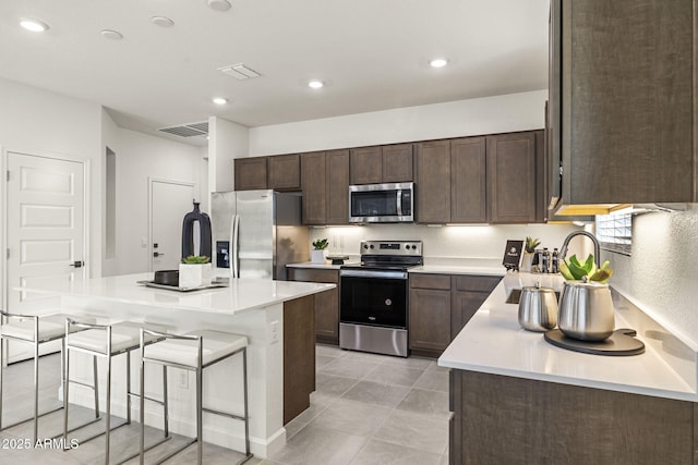 17738 W Onyx Ave, Waddell, AZ 85355 - kitchen with stainless steel appliances, a breakfast bar area, dark brown cabinetry, light countertops, and a kitchen island