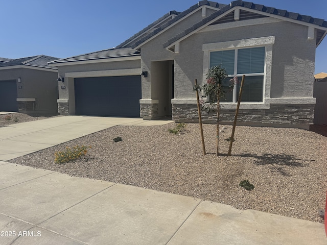 17738 W Onyx Ave, Waddell, AZ 85355 - view of front facade with concrete driveway, a garage, a tile roof, stone siding, and stucco siding