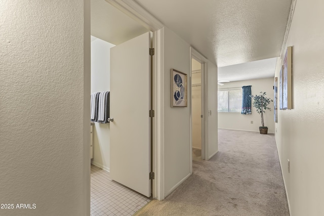 hall featuring baseboards, light carpet, a textured ceiling, and a textured wall