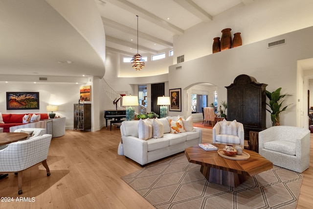 living room featuring a towering ceiling, beam ceiling, and light hardwood / wood-style floors