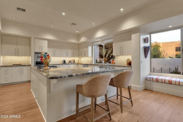 kitchen featuring a breakfast bar, white cabinetry, a center island, light hardwood / wood-style flooring, and dark stone counters