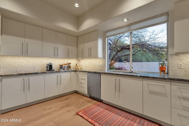 kitchen featuring sink, dark stone countertops, white cabinets, stainless steel dishwasher, and light hardwood / wood-style flooring