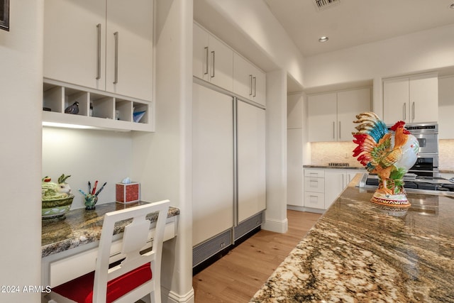 kitchen featuring double oven, dark stone countertops, white cabinets, backsplash, and light hardwood / wood-style flooring