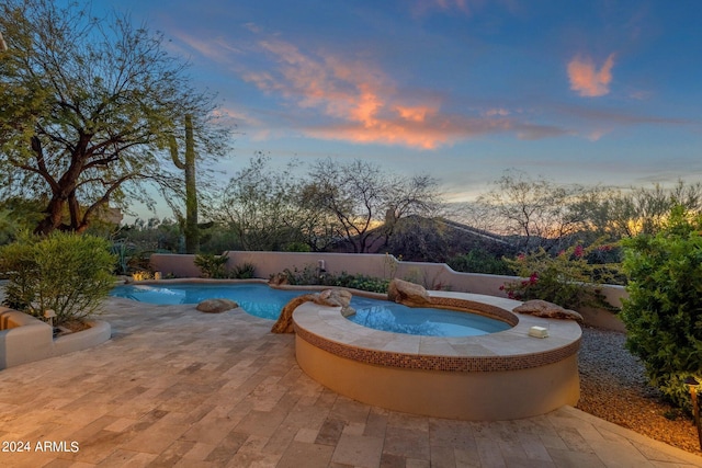 pool at dusk with an in ground hot tub and a patio area