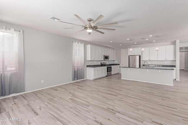kitchen featuring dark countertops, open floor plan, ceiling fan, a sink, and stainless steel appliances