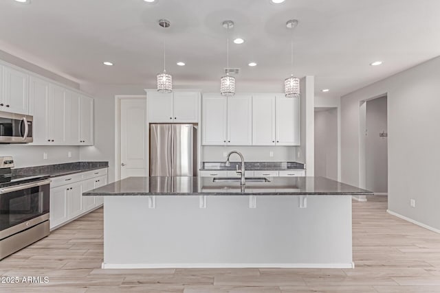 kitchen featuring a sink, dark stone counters, appliances with stainless steel finishes, and light wood finished floors