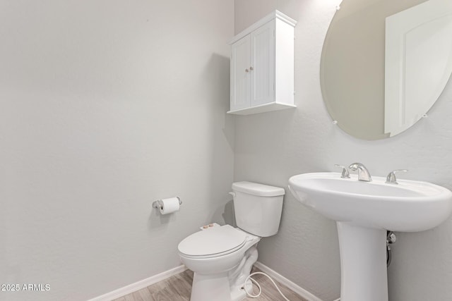 half bath featuring baseboards, a sink, wood finished floors, and toilet