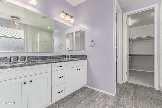 full bath with a walk in closet, a sink, double vanity, baseboards, and a shower stall