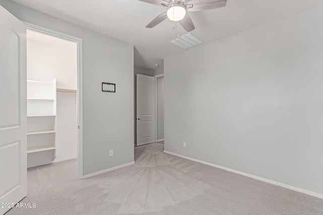 unfurnished bedroom with ceiling fan, light carpet, a walk in closet, baseboards, and a closet